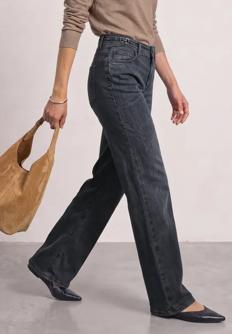 Jean à jambes larges avec des détails au niveau de la ceinture Steel Grey Washed Femme marche, porte un jean noir ample, des ballerines noires et un sac beige.