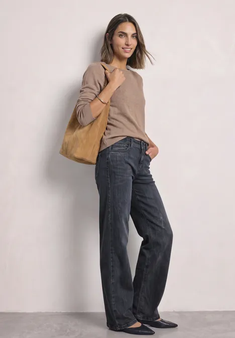Jean à jambes larges avec des détails au niveau de la ceinture Steel Grey Washed Femme en pull beige, jean large noir et ballerines, portant un cabas en daim marron devant un fond clair.
