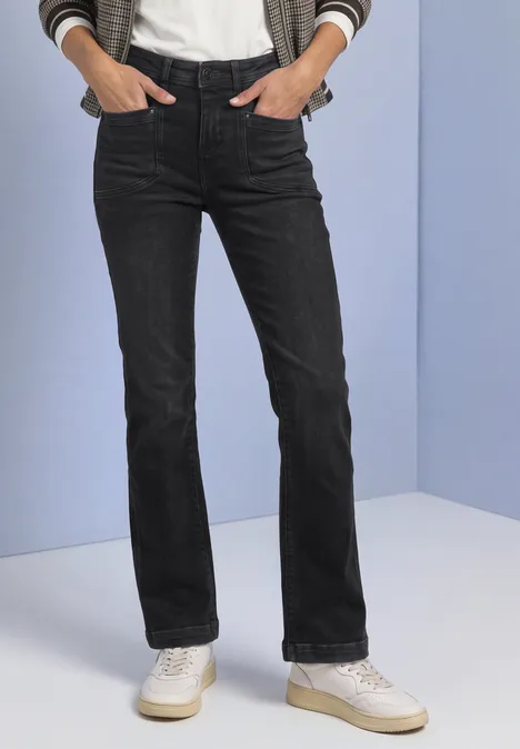 Jean bootcut taille haute, coupe slim Black Washed Schwarze Jeans mit geradem Schnitt und weißen Sneakern, Hände in den Taschen.