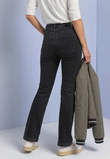 Jean bootcut taille haute, coupe slim Black Washed Rückansicht einer Person in schwarzer Schlaghose und weißem Oberteil, die einen karierten Blazer hält.
