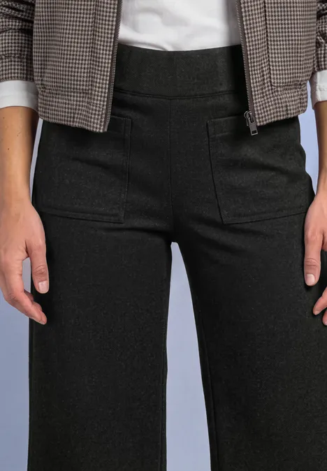 Person trägt hoch taillierte schwarze Hose, weißes Shirt und karierte Jacke.