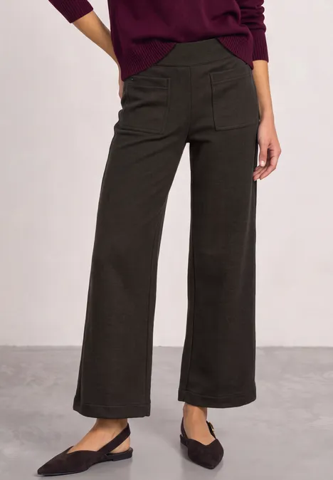 Iemand draagt een losse, donkergrijze enkellange broek met zijzakken en zwarte slingbacks.