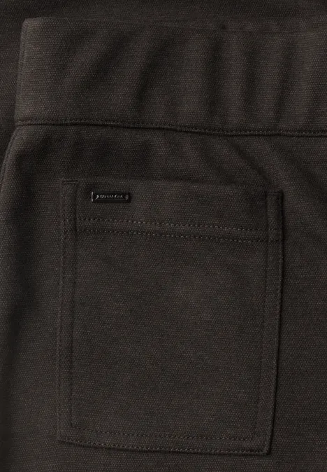Close-up van een donkere broek met een vierkante opgestikte zak en klein merkembleem.