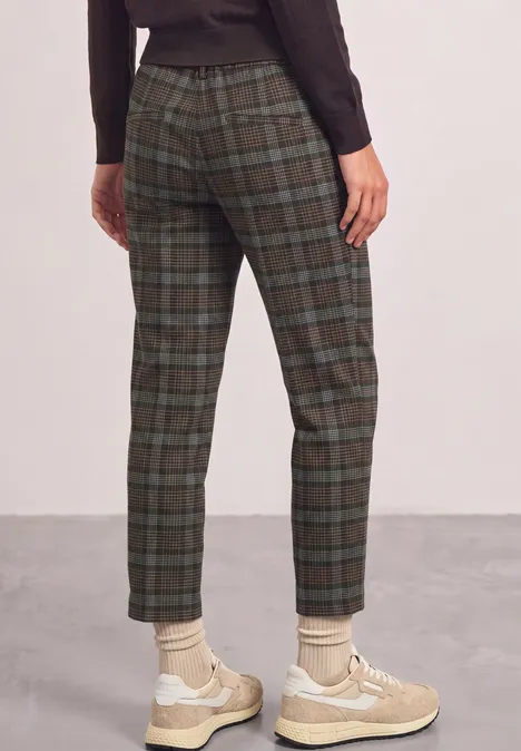 Rugaanzicht van een persoon met groengrijs geruite broek en beige sneakers.