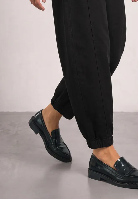 Pantalon taille haute Barrel Leg, coupe décontractée Black Ein Model trägt schwarze, glänzende Loafers zu hochgeschnittenen Hosen vor neutralem Hintergrund.