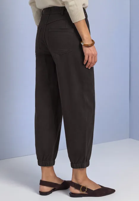 Pantalon taille haute Barrel Leg, coupe décontractée black coffee Schwarze, hoch geschnittene Hose mit elastischen Bündchen, kombiniert mit flachen braunen Slippern vor hellem Hintergrund.