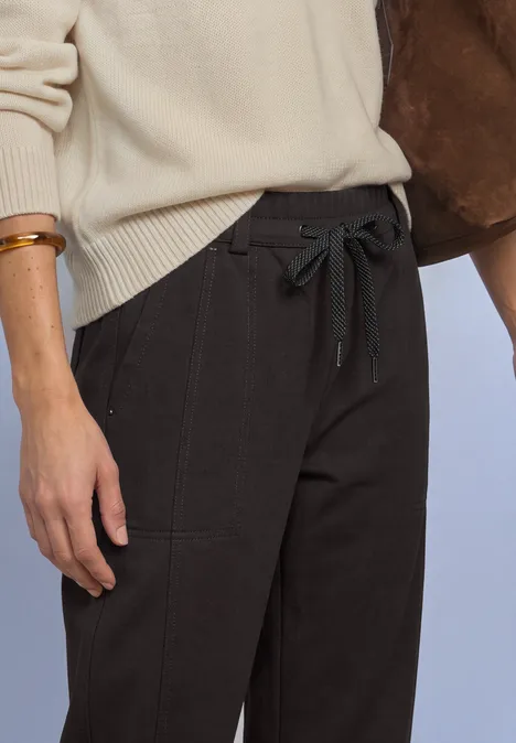 Pantalon taille haute Barrel Leg, coupe décontractée black coffee Person in beigem Pullover und schwarzen, taillierten Hosen mit Tunnelzug und Gürtelband.