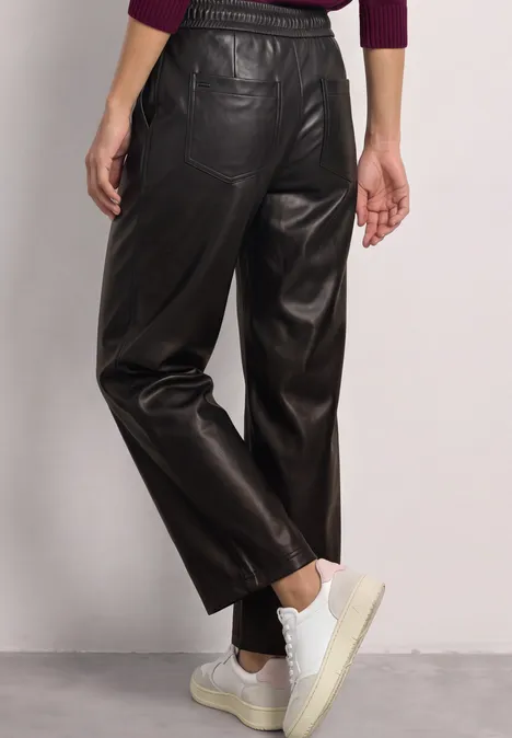 Straight Leg Hose in Leder-Optik black coffee Rückansicht einer schwarzen, hochgeschnittenen Lederhose mit weitem Bein und weißen Sneakern.
