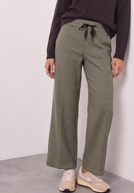 Damenhose in Olivgrün mit weitem Bein und schwarzem Kordelzug, kombiniert mit einer dunklen Oberbekleidung.