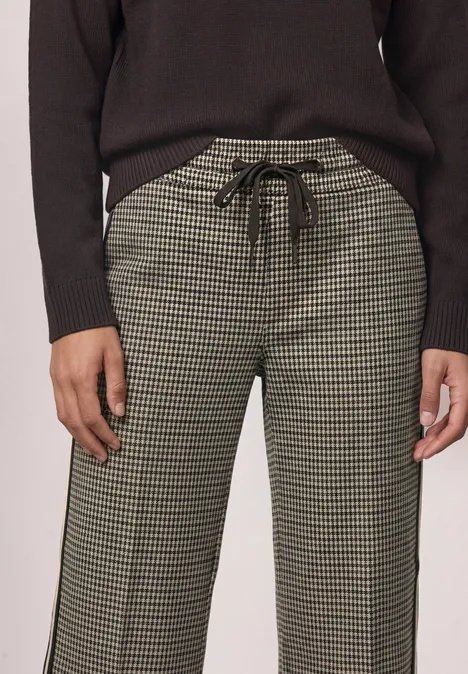Eine Person trägt eine Hose im Hahnentritt-Muster mit Tunnelzug und einen schwarzen Pullover.