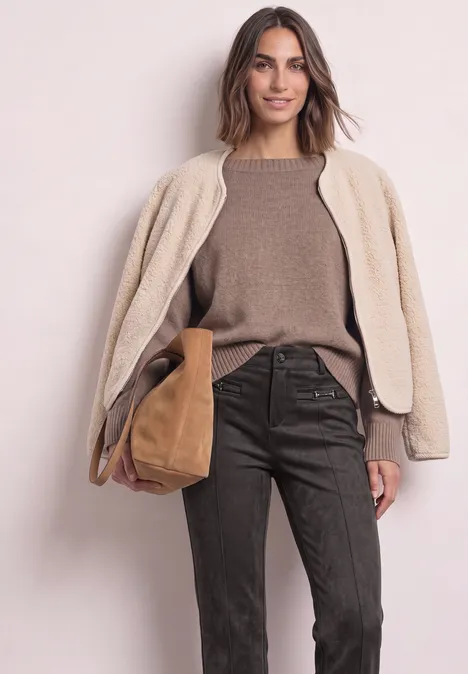 Bootcut Velourshose im Slim Fit black coffee Frau in beigem Teddy-Mantel, braunem Pullover und dunkelbrauner Hose mit brauner Tasche vor hellem Hintergrund.