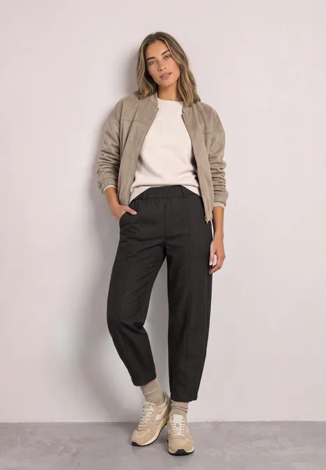 High Waist Barrel Leg Hose im Casual Fit black coffee Eine Frau in legerer Kleidung: Bomberjacke, weißes Shirt, schwarze Hose und Sneaker vor neutralem Hintergrund.
