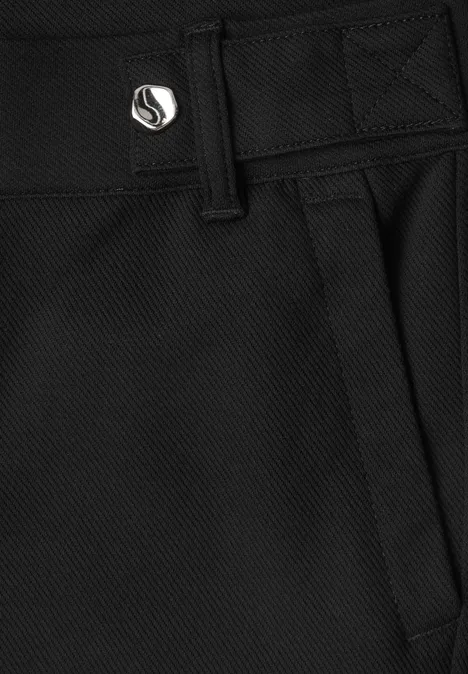 Close-up van een zwarte, gestructureerde broek met riemlussen, zijzak en metalen knoop met logo.