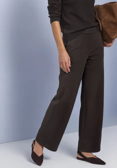 Wijde donkerbruine broek met puntige slingback-pumps, gecombineerd met een bruine tas