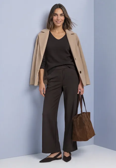 Vrouw in zakelijke outfit met beige blazer, zwart topje, wijde broek, ballerina's en bruine tas.