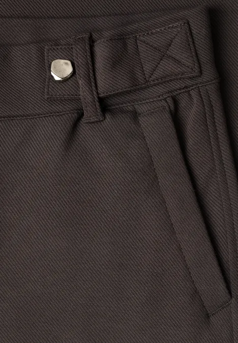 Close-up van een donkerbruine broek met riemlussen, zakopening en zichtbare naden.