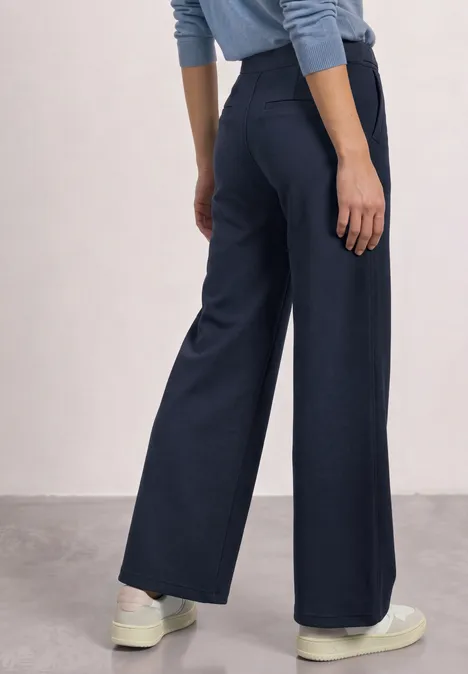 Donkerblauwe, wijde broek met hoge taille, gecombineerd met witte sneakers. Achteraanzicht.