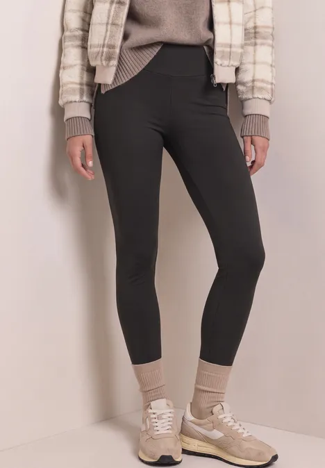 Thermo-Leggings im Skinny Fit black coffee Schlanke Person in schwarzen Leggings, beigen Socken, Sneakern und karierter Jacke vor hellem Hintergrund.
