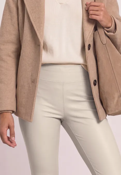Nahaufnahme: Person trägt beigen Blazer, helles Top und cremefarbene, enge Hosen mit passender Tasche.