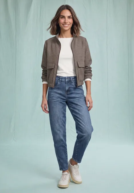 High Waist Barrel Leg Jeans im Loose Fit Medium Blue Destory Washed Frau in Jeans, weißem T-Shirt, olivgrünem Blouson und Sneakern vor hellem Hintergrund.