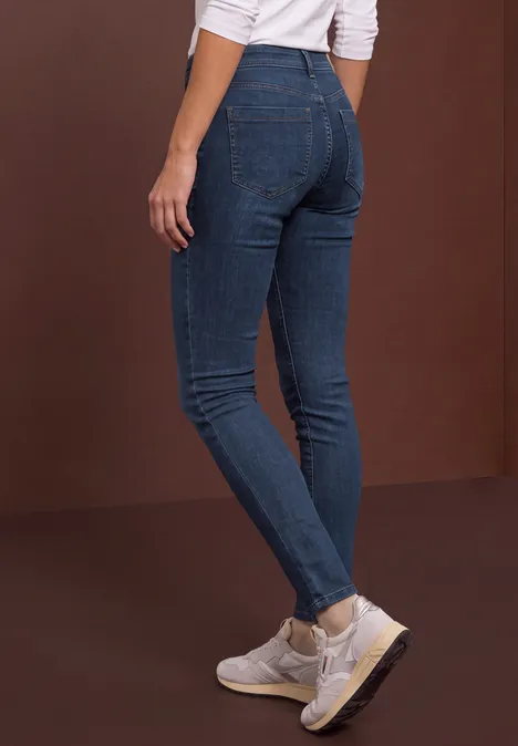 Personne porte un jean skinny bleu foncé et des baskets blanches sur fond marron.