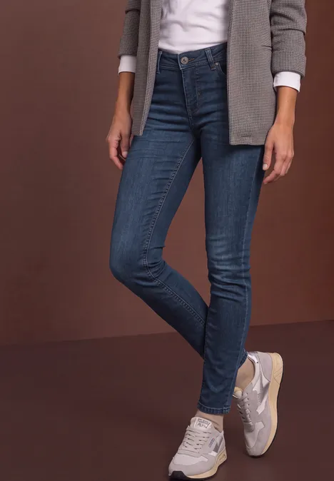 Femme en jeans skinny bleu, baskets blanches, chemise blanche et veste grise
