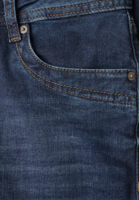 Gros plan d'un jean bleu montrant une poche, des coutures et des rivets métalliques.