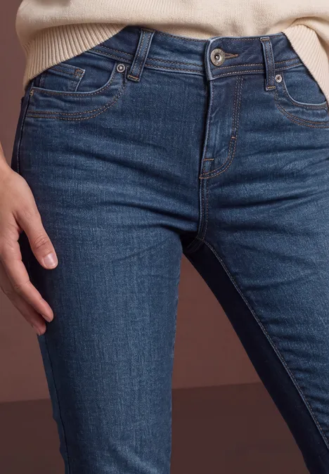 Nahaufnahme einer Person in dunklen Jeans mit der Hand auf der Hüfte vor neutralem Hintergrund.