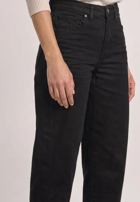 Schwarze High-Waist-Jeans an Person, Fokus auf Hüfte und Oberschenkel.