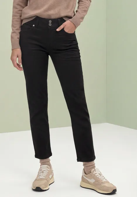 Person in schwarzen Jeans und beigen Sneakern vor hellem, minimalistischem Hintergrund.