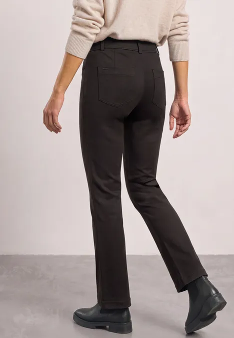 High Waist Bootcut-broek met Slim Fit-pasvorm black coffee Person von hinten in dunkler Hose, beigefarbenem Pullover und schwarzen Stiefeln vor hellem Hintergrund.