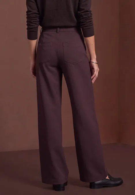 Mid Waist broek met rechte pijpen in casual pasvorm berry plum Frau von hinten in braunen, weiten Hosen und schwarzen Schuhen vor braunem Hintergrund.
