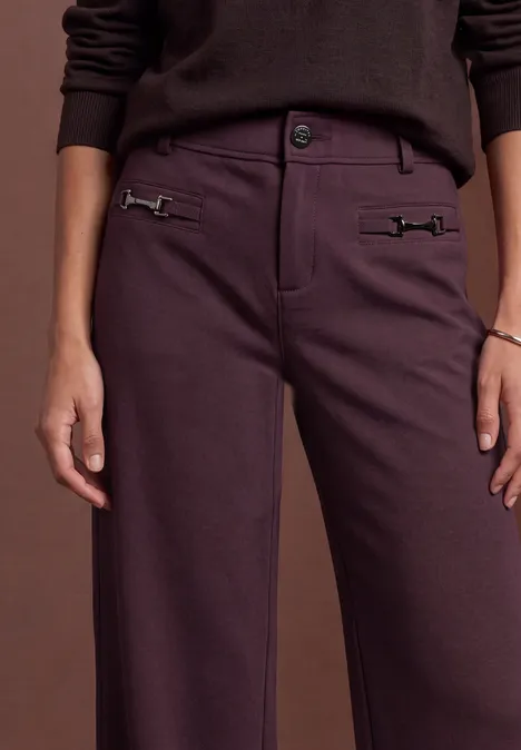 Mid Waist broek met rechte pijpen in casual pasvorm berry plum Oberkörper einer Person in braunem Pullover und plumafarbener Hose mit seitlichen Zierschnallen.