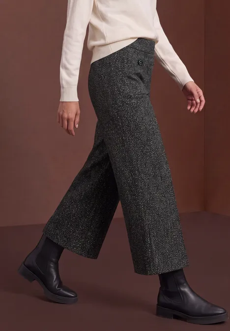 Zijaanzicht van wijde grijze wollen broek, zwarte enkellaarzen en witte top.