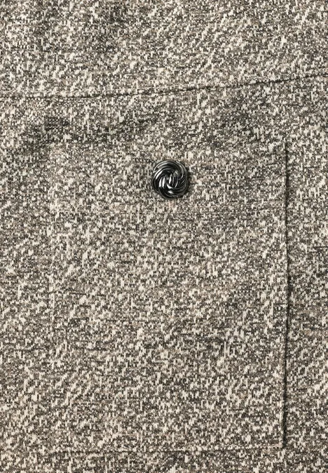 Grijze, gestructureerde stof met zwarte knoop en zichtbare naad van een zak.