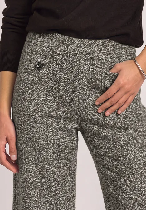 Grijze tweedbroek met hoge taille en subtiel motief, hand op de heup.