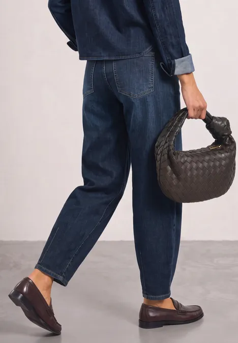 Relaxed Barrel Leg Jeans im Loose Fit Dark blue authentic washed Person im dunklen Jeans-Outfit (Jacke & Hose), trägt geflochtene Handtasche und braune Loafers.