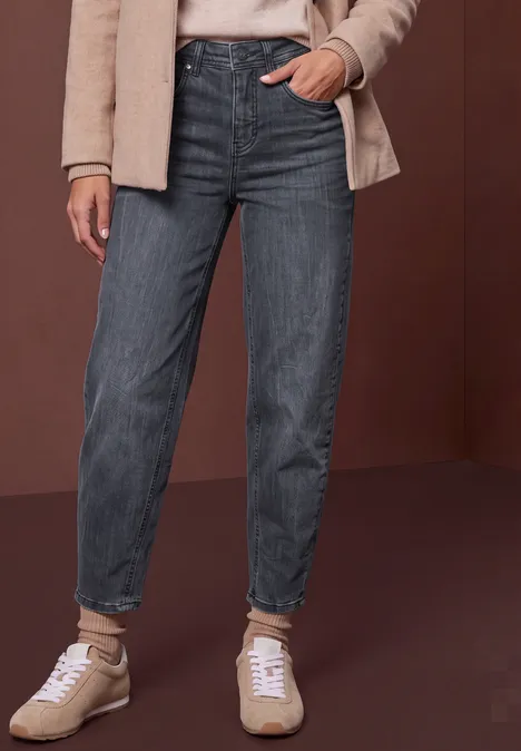 Vue partielle d'une personne portant un jean droit gris foncé retroussé aux chevilles, sneakers beiges et veste claire.