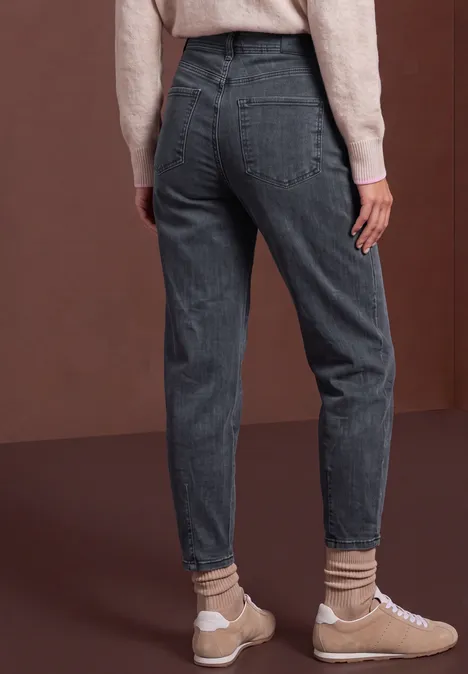 Vue arrière d’une personne portant un jean gris taille haute, chaussettes et baskets beiges sur fond marron.