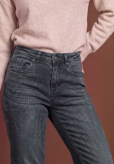 Person en pull clair et jean taille haute effet délavé foncé, gros plan sur la taille.