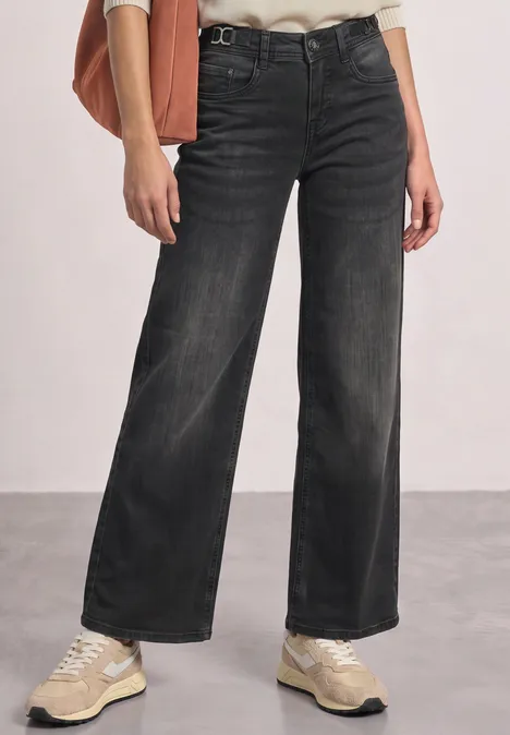 Mid Waist Wide Leg Jeans im Loose Fit Black Washed Schwarz-graue, weit geschnittene Jeans mit hellen Sneakern vor neutralem Hintergrund.