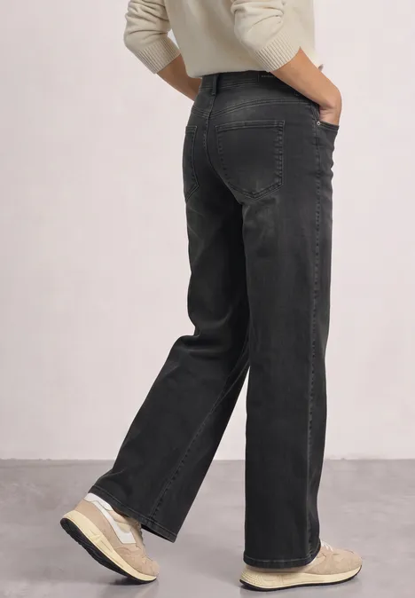 Mid Waist Wide Leg Jeans im Loose Fit Black Washed Schwarze Jeans mit weiten Beinen, Person von hinten, Hände in Taschen, dazu helle Sneaker.