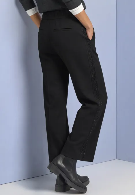 Mid Waist Straight Leg Hose im Loose Fit Black Schwarze, weite Hose mit geradem Bein und schwarzen Stiefeletten vor einem pastellfarbenen Hintergrund.