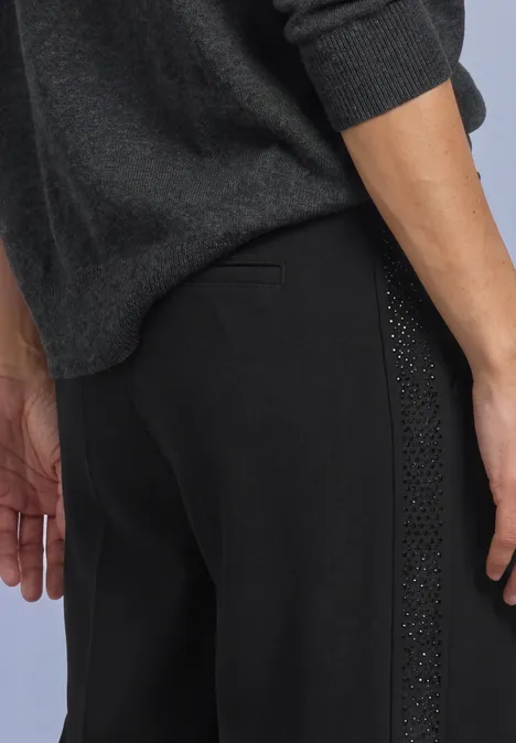 Mid Waist Straight Leg Hose im Loose Fit Black Seitliche Ansicht einer Person in schwarzer Hose mit Nietenverzierung und dunkelgrauem Pullover.