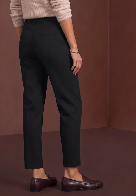 Pantalon tailleur noir, coupe droite cheville, associé à des mocassins marron.