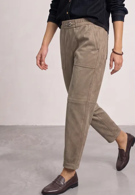 Une personne porte un pantalon taille haute beige en velours côtelé, ceinturé, et des mocassins marron foncé.
