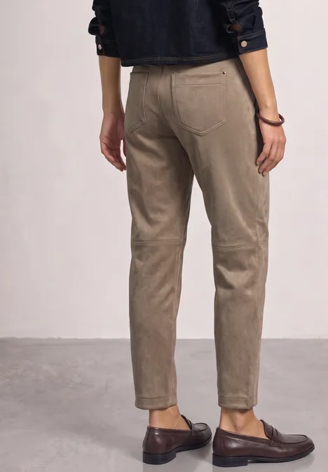 Personne vue de dos portant un pantalon beige et des mocassins marron foncé sur fond neutre.