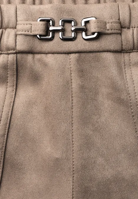Gros plan d'un pantalon en daim beige clair avec une chaîne argentée à la taille