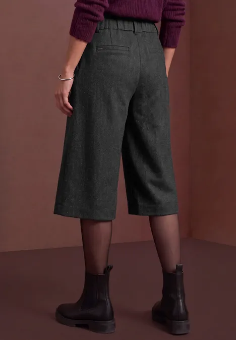 Bermuda met High Waist en Wide Leg pijpen in casual pasvorm Black Rückansicht einer Person in schwarzen Culotte-Hosen, transparenten Strumpfhosen und schwarzen Boots vor braunem Hintergrund.