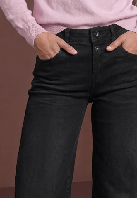 Mid Waist Jeans Culotte im Loose Fit black authentic washed Schwarze High-Waist-Jeans mit weitem Bein, Hände stecken in den Taschen einer rosa Bluse.